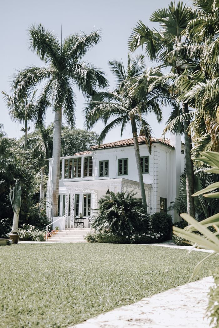 Elegant mansion surrounded by lush gardens and palm trees under the sun.